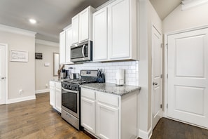 A kitchen with white cabinets, a stainless steel microwave, a gas stove, and a tiled backsplash.