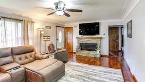 A spacious living room with a large leather sofa, a fireplace, and a ceiling fan. - Port Clinton Home: Hot Tub, Steps to Portage River (Port Clinton)