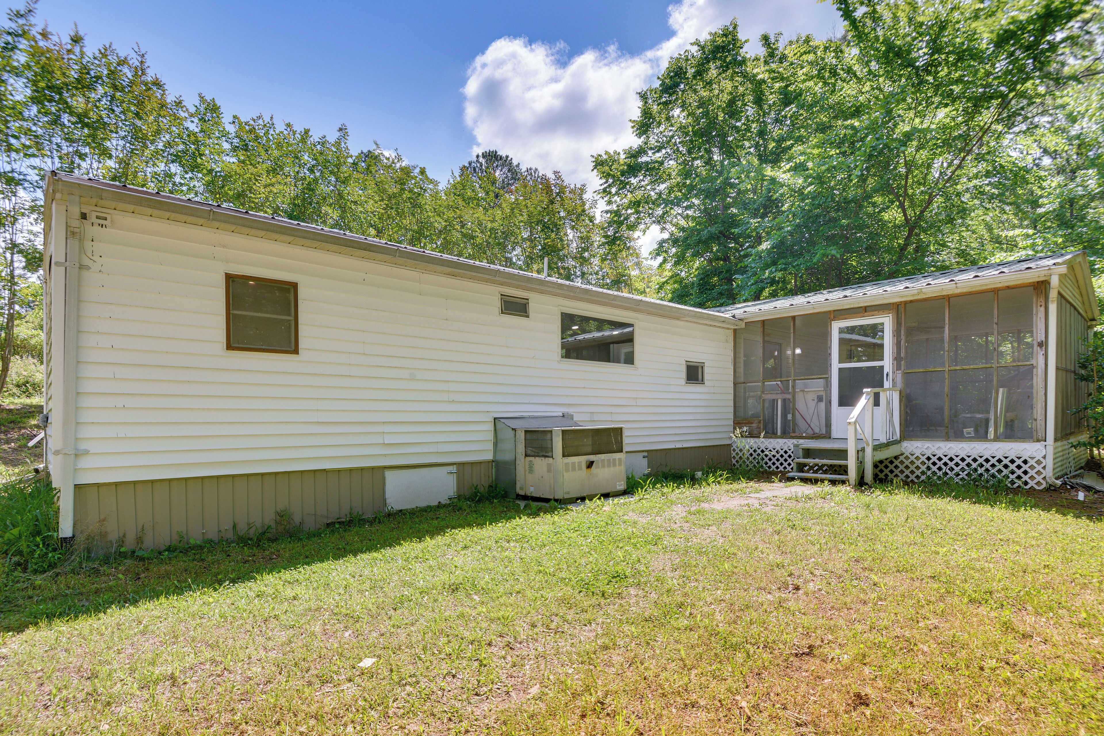A mobile home with a small porch and a screened area, surrounded by a grassy yard and trees.