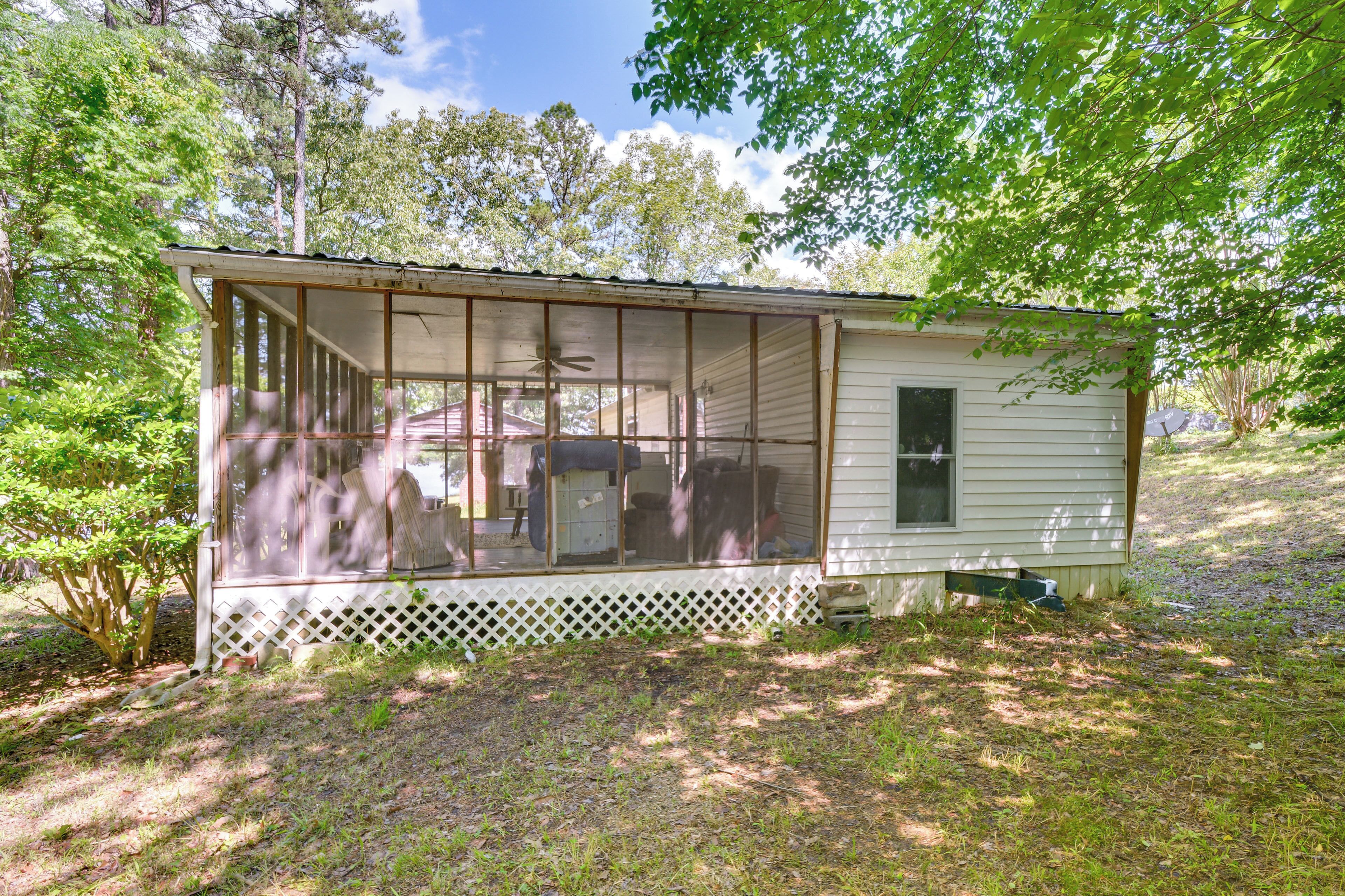 A small, single-story cabin with a screened porch, surrounded by trees and a grassy yard.