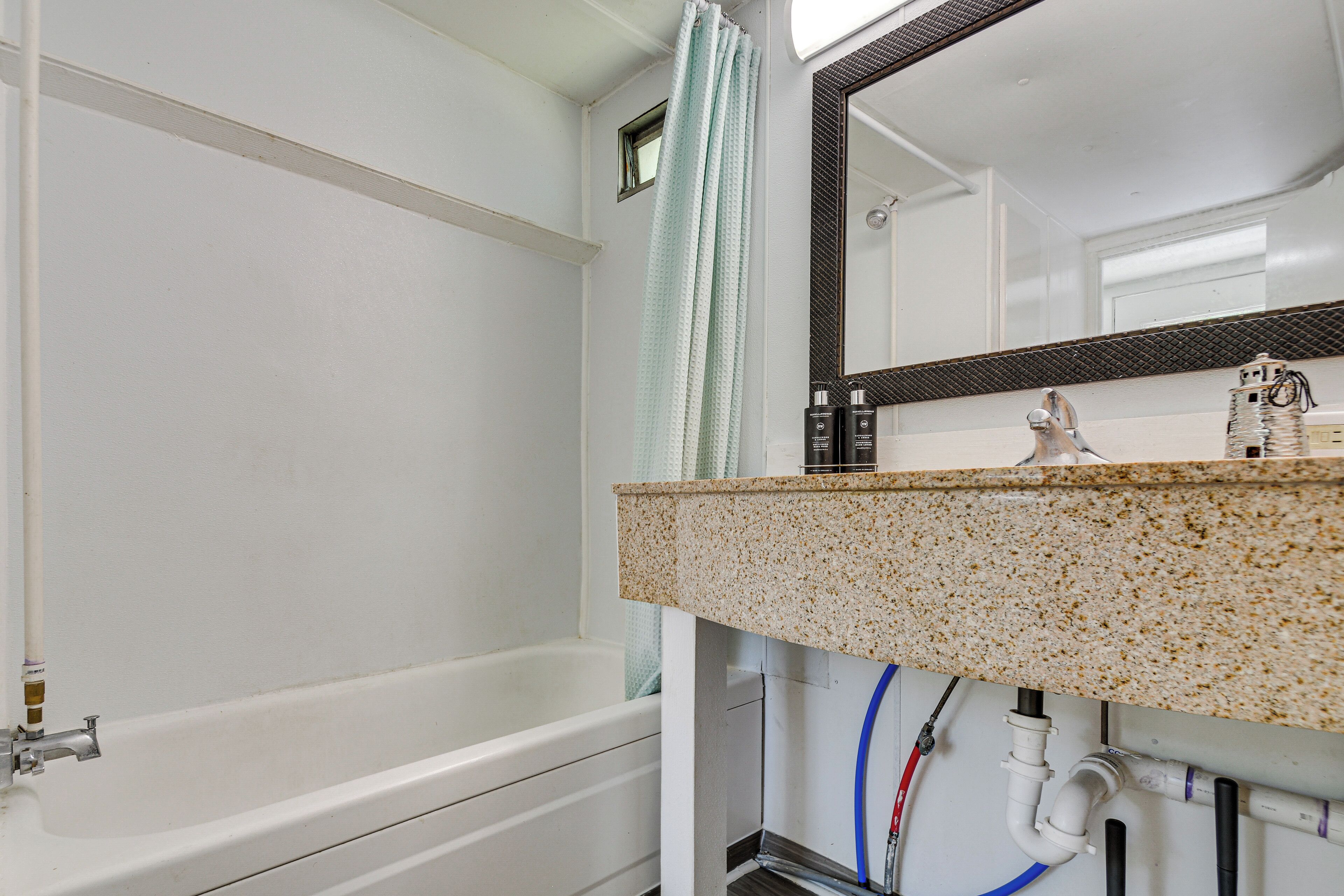 A bathroom with a white bathtub, a granite countertop, and a mirror with a black frame.