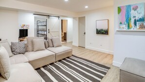 A modern living room with a beige sectional sofa, a striped rug, and a bunk bed in the background. - Pine Cabin w/ Large Deck & Scenic Mountain Views! (Pine)