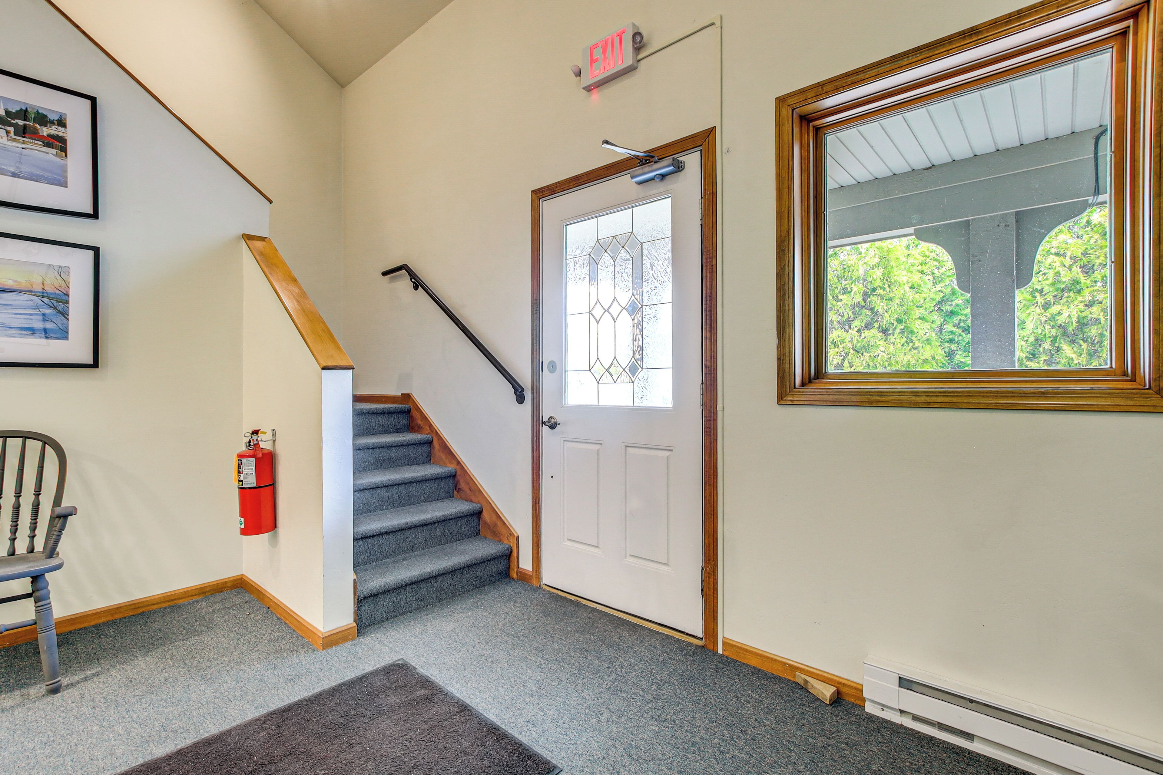 A staircase leading to a door with a glass panel, a fire extinguisher, and framed pictures on the wall.