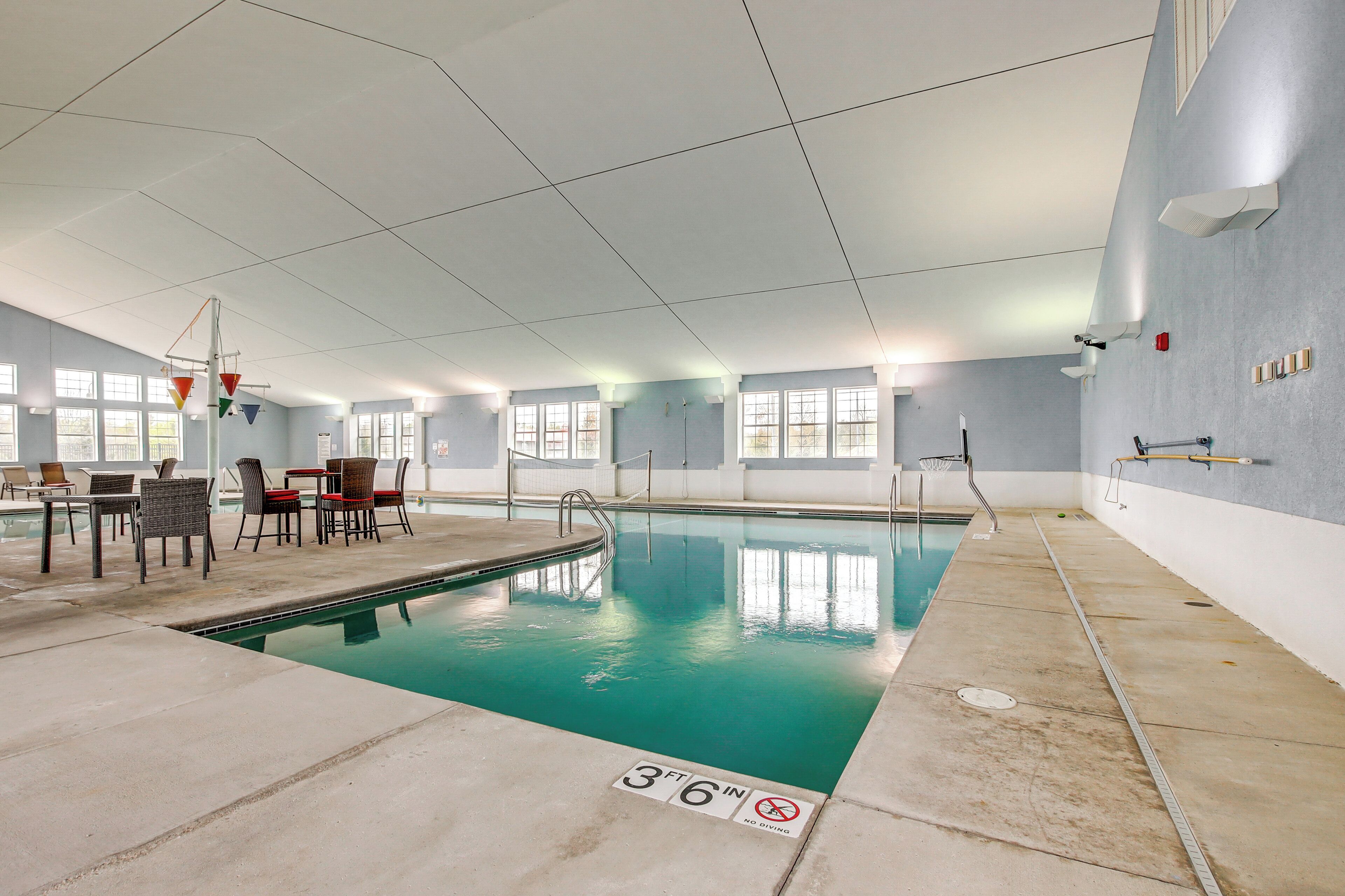An indoor swimming pool with a 3'6" depth marker, surrounded by lounge chairs and tables, with windows along the walls.