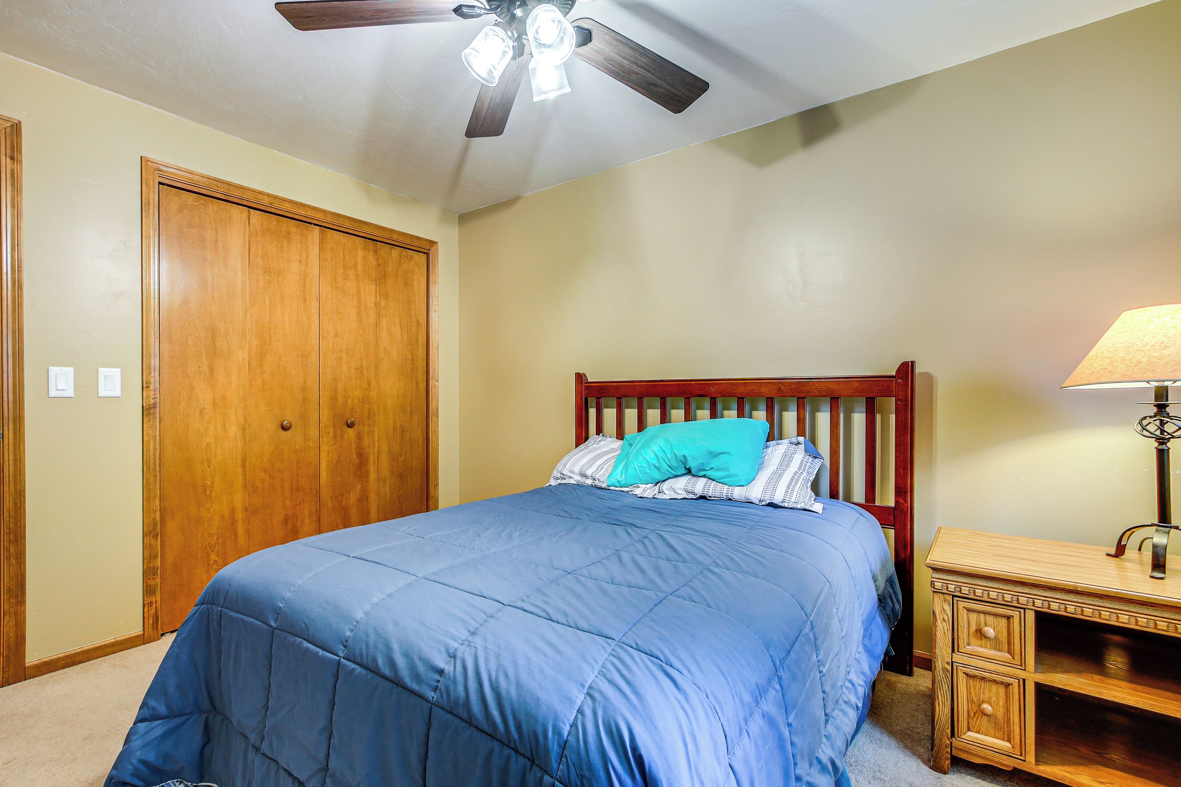 A bedroom with a bed, wooden wardrobe, ceiling fan, and bedside table.