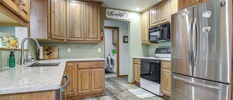 Una cocina con armarios de madera, un refrigerador de acero inoxidable, un microondas y una lavadora.