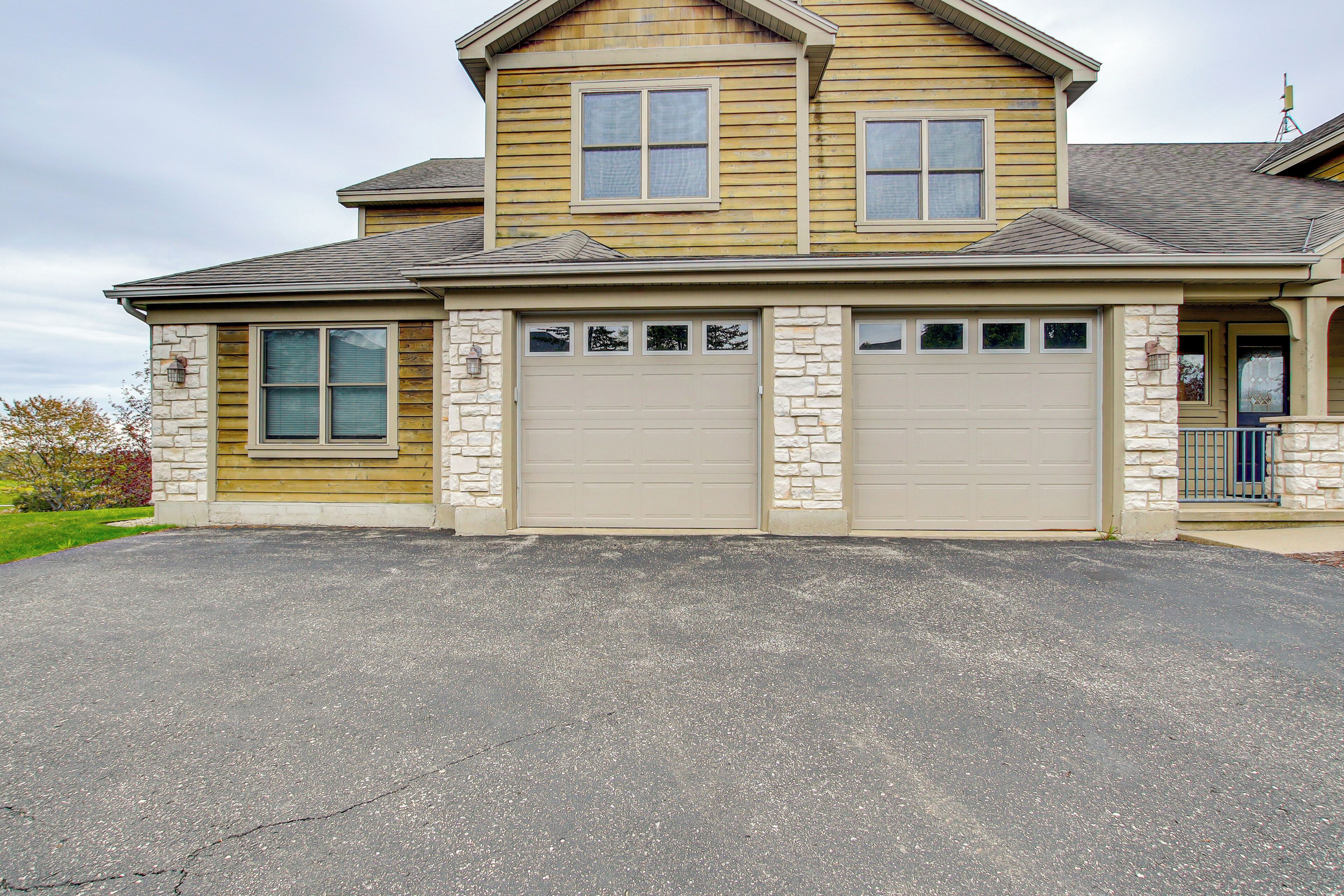 Une maison à deux étages avec un garage, une façade en pierre et une allée.
