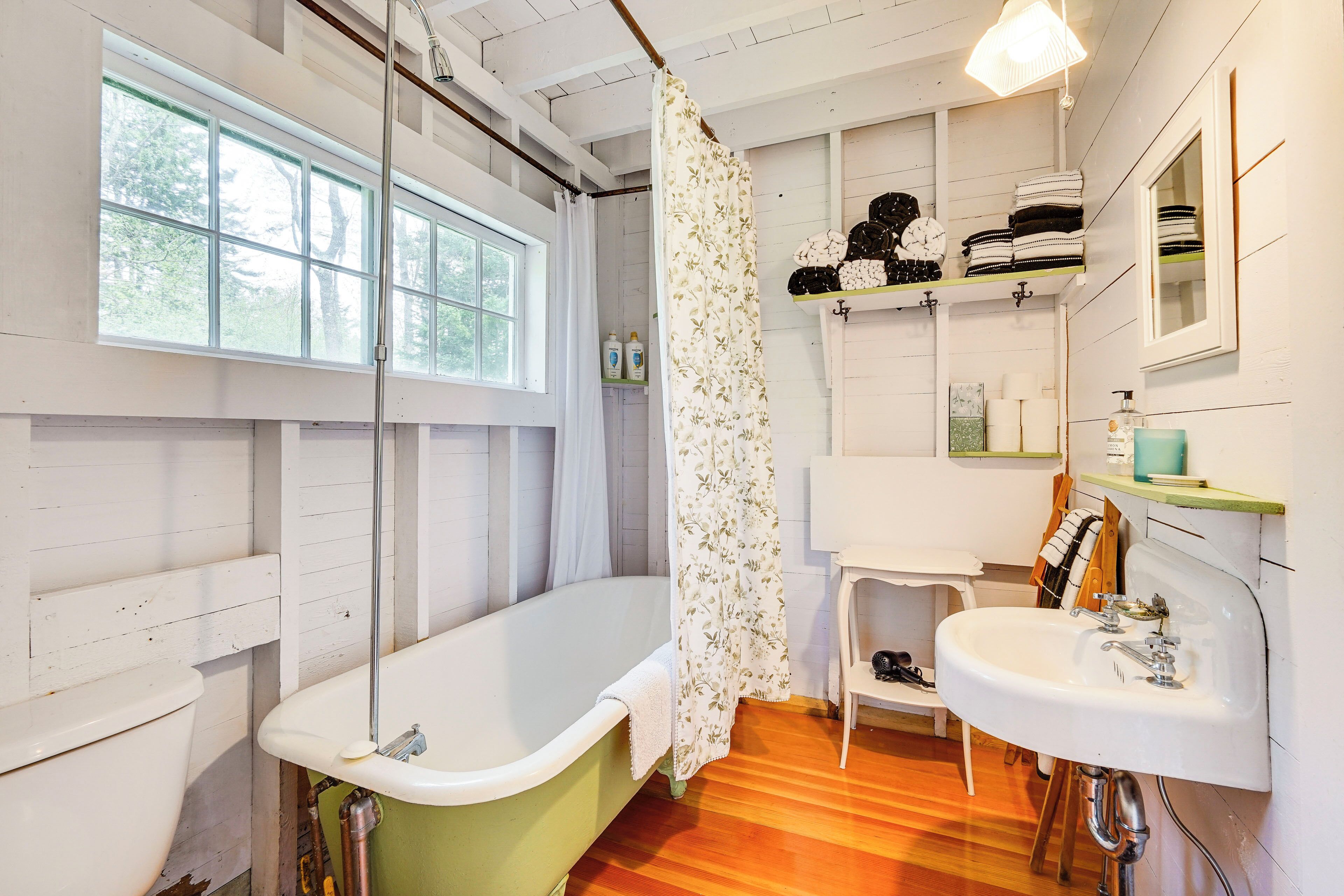 A bathroom with a bathtub, a sink, a window, and shelves with towels.