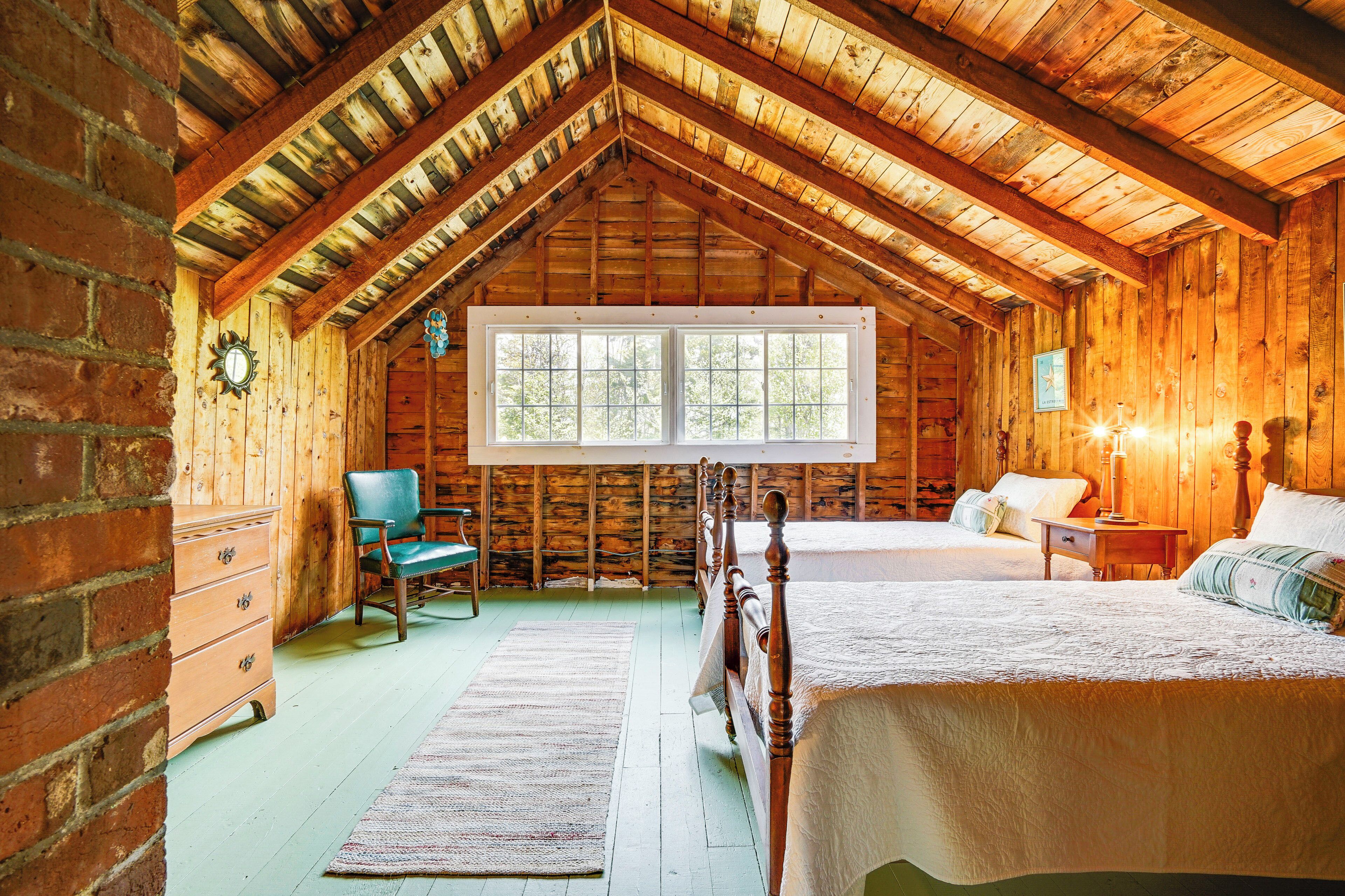 A log cabin bedroom with a large window, wooden furniture, and a bed with white bedding.