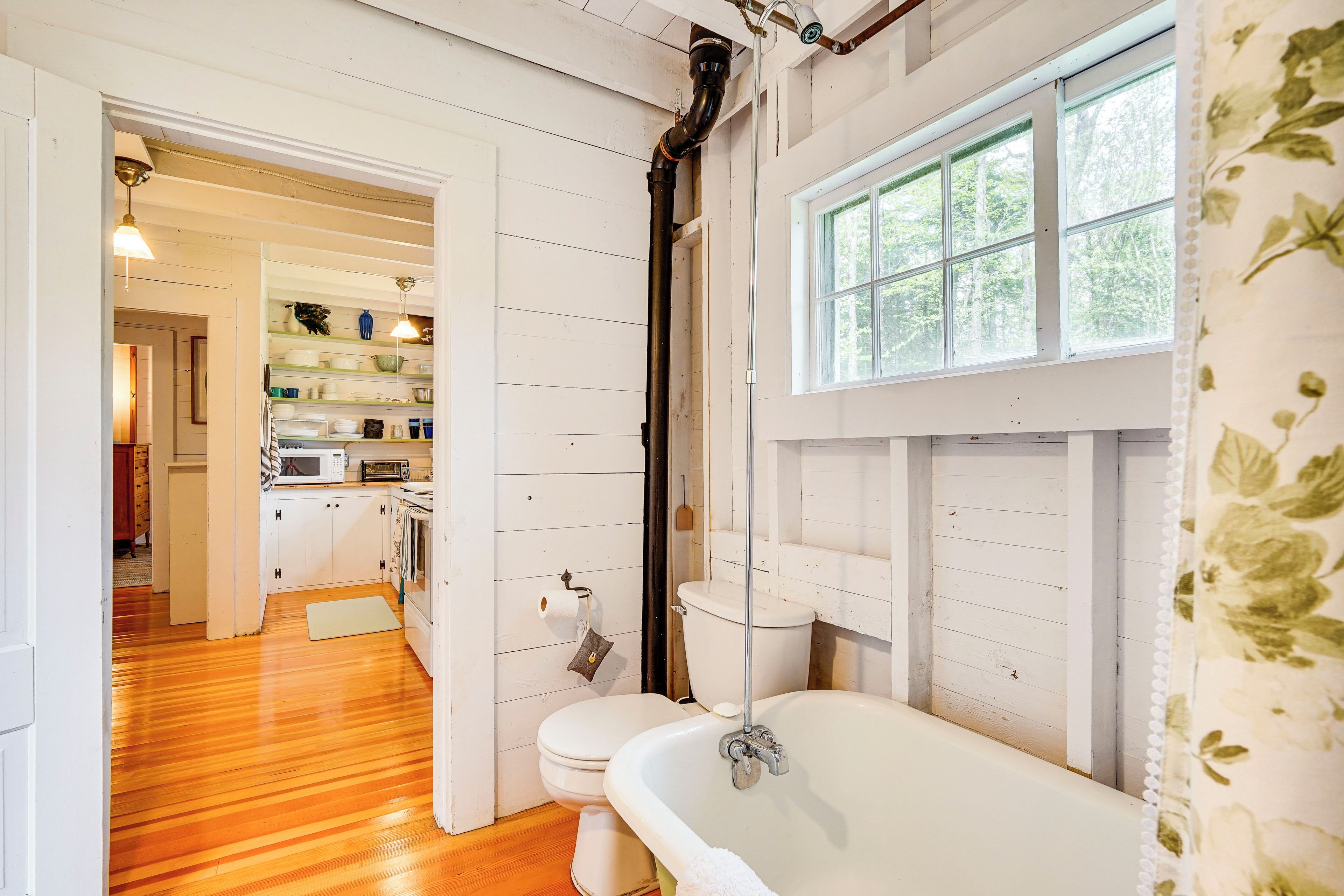 A bathroom with a white bathtub, toilet, and sink. There is a window with a view of trees.