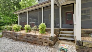 A covered porch with a wooden bench, a red door, and a small garden area with shrubs and a gravel path. - Tennessee Mountain Cabin ~ 18 Mi to Knoxville! (Strawberry Plains)