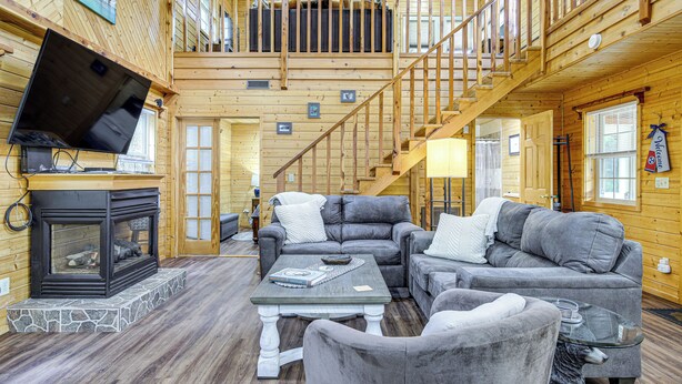 A spacious living area with a fireplace, grey sofas, a coffee table, and a staircase leading to an upper level. - Tennessee Mountain Cabin ~ 18 Mi to Knoxville! (Strawberry Plains)
