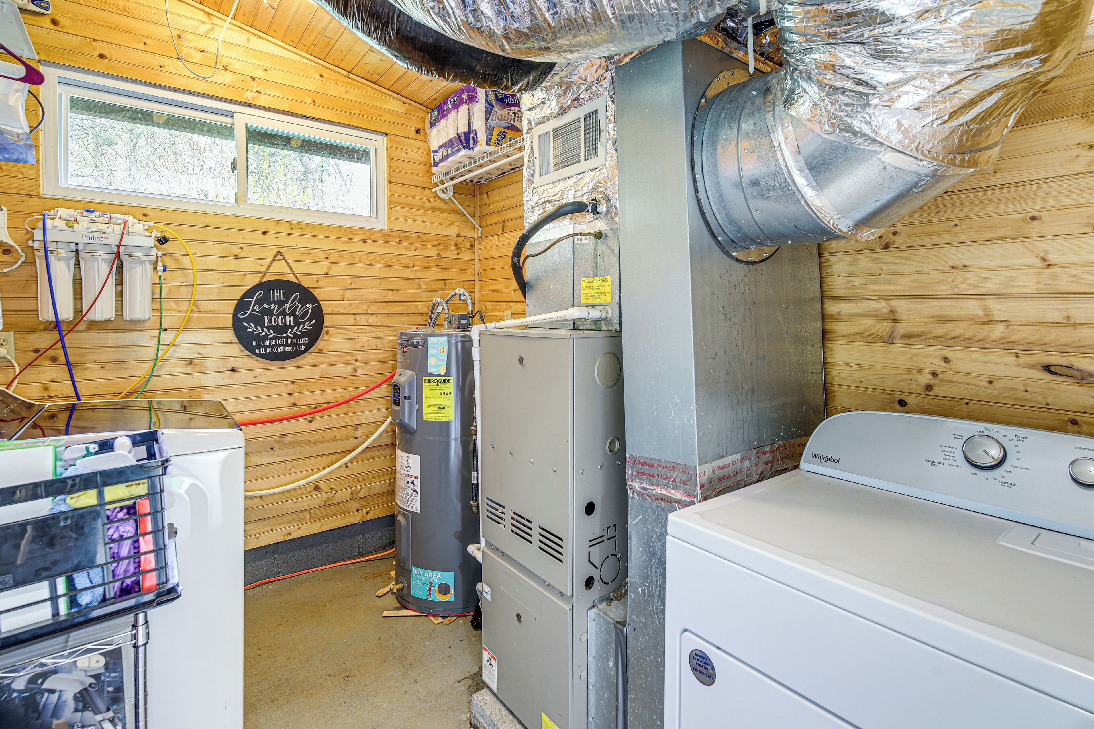 Una sala de lavandería con una lavadora Whirlpool, un secadora apilada y un calentador de agua.