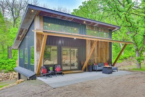 A modern cabin with a large glass door, wooden deck, and outdoor seating area. - Modern Louisville Home on 3 Acres w/ Gas Fire Pit! (Louisville)