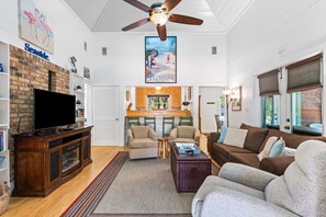 Ein Wohnzimmer mit Fernseher, Kamin, Sitzecke und Deckenventilator.