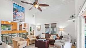 A spacious living area with a ceiling fan, a kitchen bar, and a large Florida-themed poster. - Beautiful Original Seaside Cottage + Swim & Tennis Club: Sleeps 6 (Santa Rosa Beach)