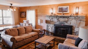 A cozy living room with a stone fireplace, leather sofas, and a wooden floor.