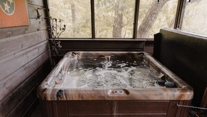A hot tub with a wooden interior, a window with a view of trees, and a decorative plant beside it.