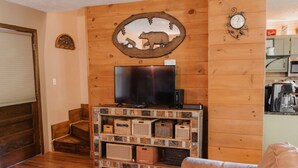 A living room with a wooden wall, a TV on a wooden stand, and a staircase.