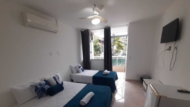 A hotel room with two beds, a ceiling fan, an air conditioning unit, a TV, and a view of the outdoors. - Pousada Paraiso Barra da Tijuca (Rio de Janeiro)