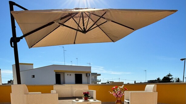 An outdoor patio with wicker furniture, a table, and a large umbrella. - welcoming suite, a few kilometers from the sea (Gagliano del Capo)