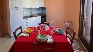 A compact kitchen with white cabinets and a red dining table set for four. - welcoming suite, a few kilometers from the sea (Gagliano del Capo)