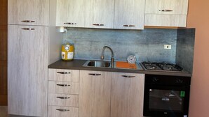 A modern kitchen with light wood cabinets, a stainless steel sink, a yellow water dispenser, a gas stove, and a black dishwasher. - welcoming suite, a few kilometers from the sea (Gagliano del Capo)