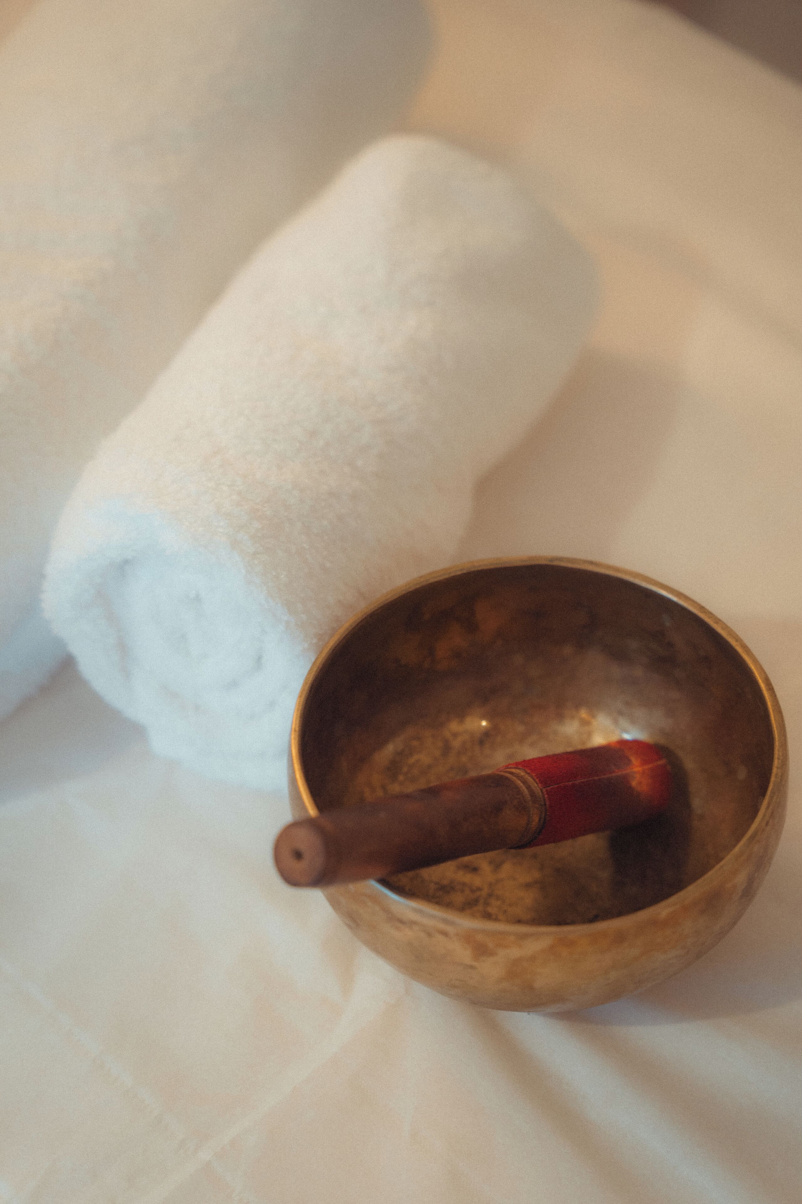 Une serviette blanche roulée et un bol en bois contenant un objet rouge, le tout posé sur une surface blanche.