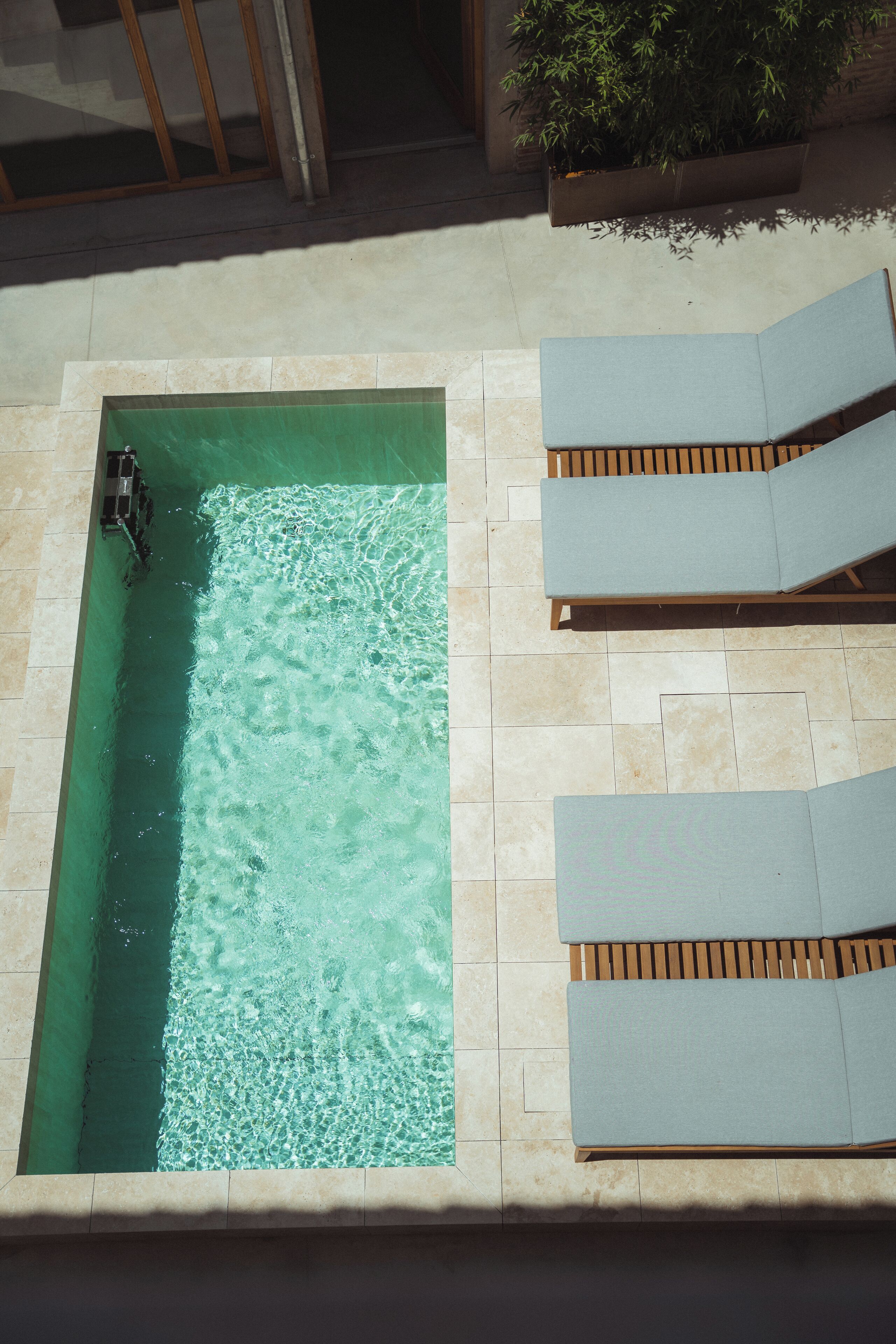 A rectangular swimming pool with clear water, surrounded by tiled flooring and wooden loungers.