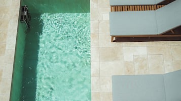 A rectangular swimming pool with clear water, surrounded by tiled flooring and wooden loungers.