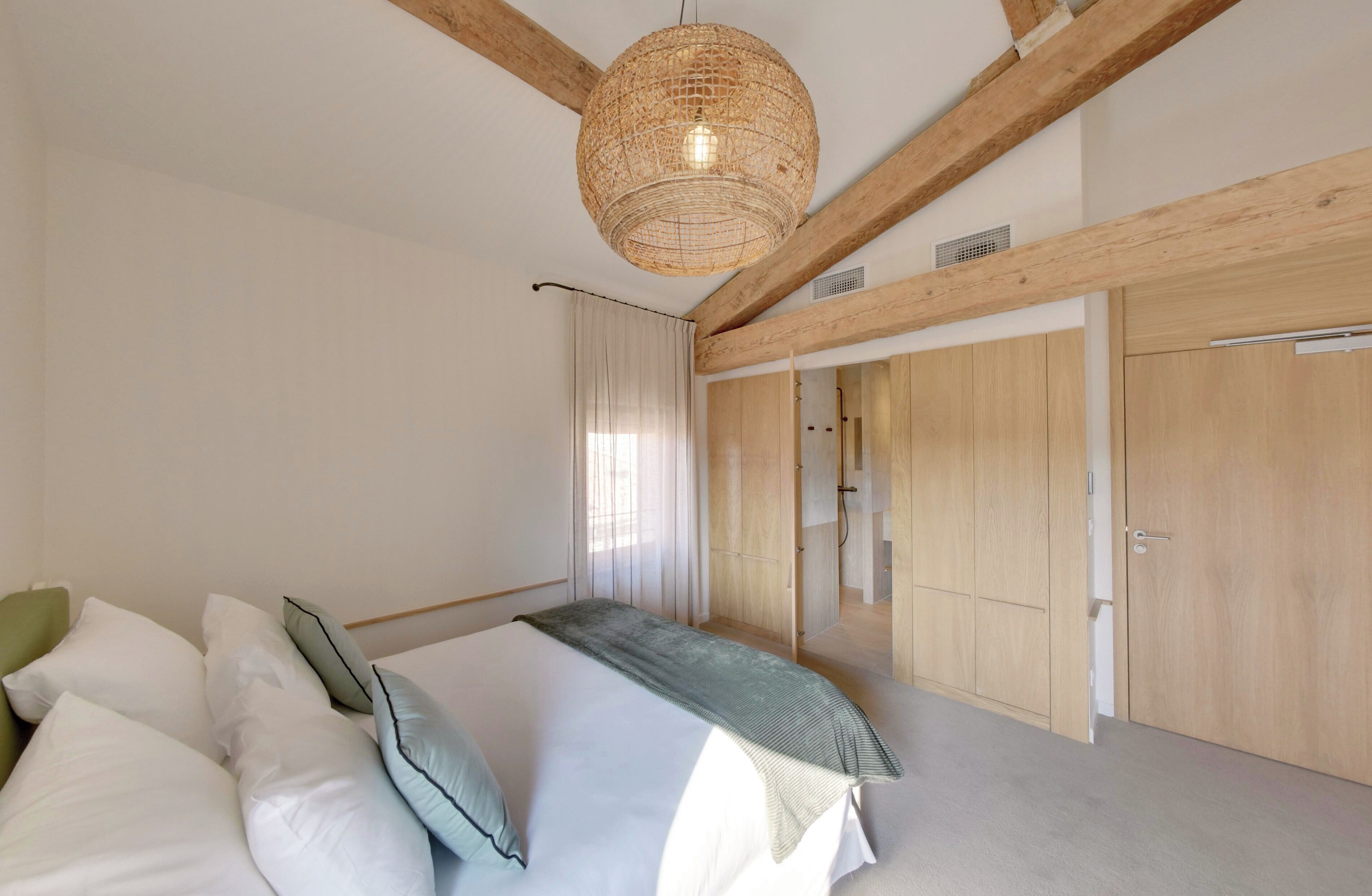 Un dormitorio con cama, lámpara colgante, vigas de madera y armario.