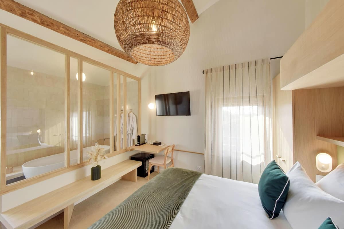 Habitación de hotel moderna con un espejo grande, una cama con ropa de cama verde y blanca, un escritorio de madera, una silla y un televisor.