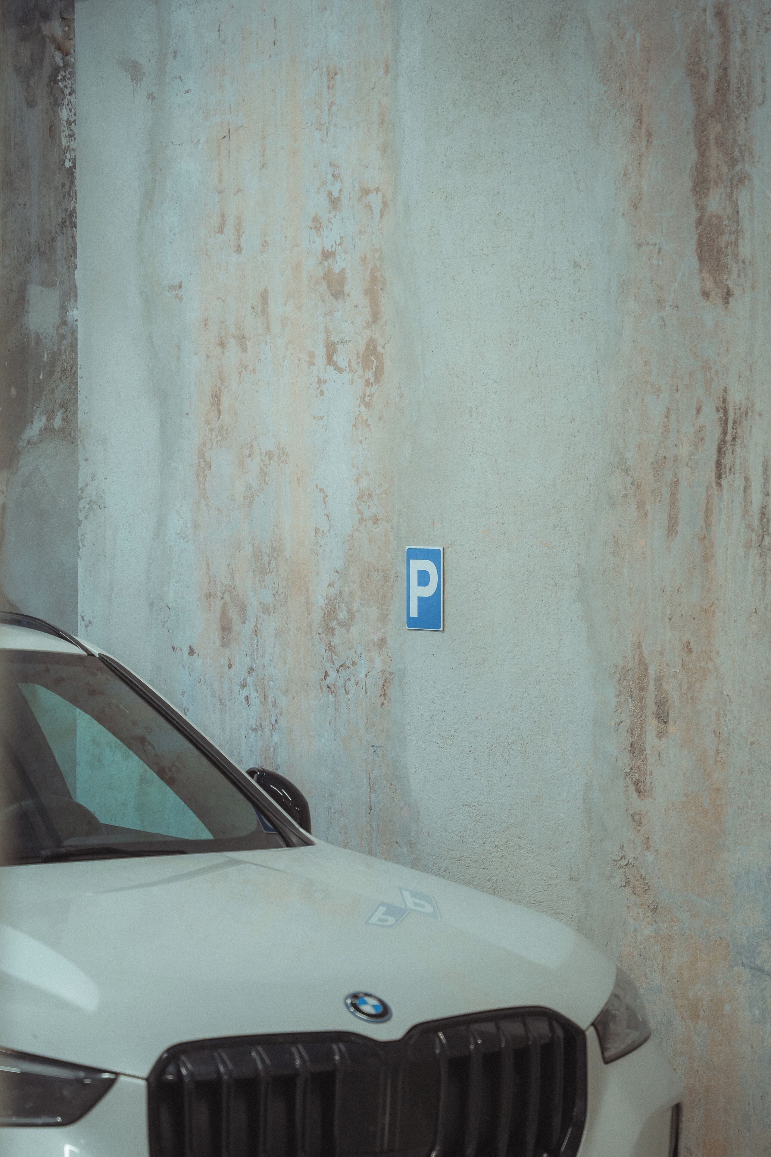 A white car parked in a garage with a visible parking sign.