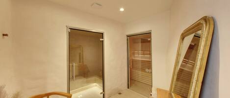 A modern bathroom with glass doors, a wooden chair, and a large mirror.