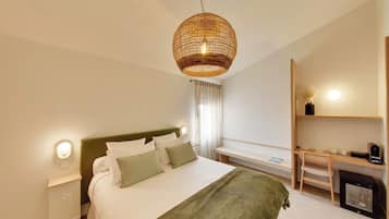 A hotel room with a bed, bedside table, lamp, desk, chair, and a small fireplace.