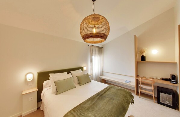 A hotel room with a bed, bedside table, lamp, desk, chair, and a small fireplace. - La Maison Gaïa Hôtel & Spa (Torreilles)