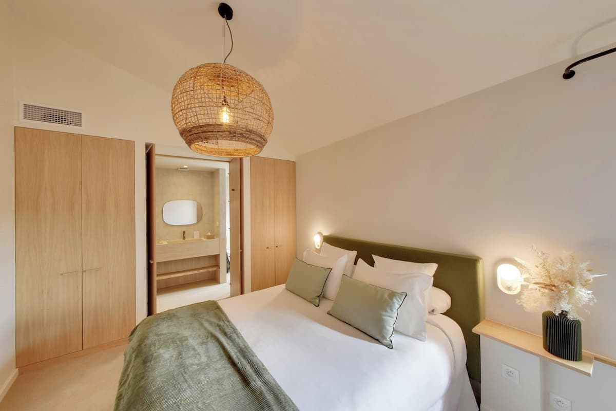 Un dormitorio moderno con una cama grande, un armario de madera, un espejo y una mesita de noche con un florero.