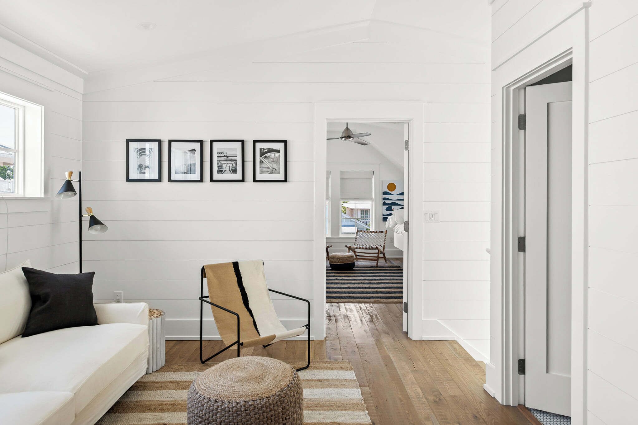 Una sala de estar moderna con un sofá blanco, una silla y una alfombra. Hay cuadros en la pared y un ventilador de techo.