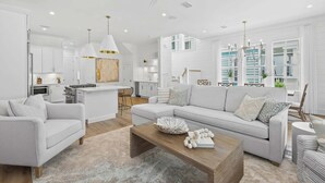 A modern living room with a sofa, coffee table, and a dining area with a kitchen in the background. - Beautiful Seacrest Home, Sleeps 16 - Lagoon Pool and Beach Tram Service (Panama City Beach)