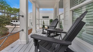 A covered porch with two Adirondack chairs and a small table, white exterior walls, and a view of a white SUV parked outside. - Bee/zhoo Small & Elegant (Santa Rosa Beach)