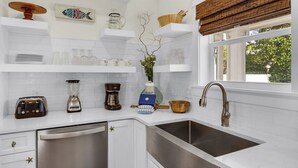 A kitchen with white cabinets, a stainless steel sink, a toaster, a blender, a coffee maker, and a vase with a branch. - Bee/zhoo Small & Elegant (Santa Rosa Beach)