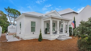 A white two-story house with a covered porch, a small front yard with mulch, and an American flag.