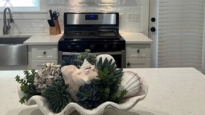 A kitchen with a stainless steel range hood, a built-in oven, and a decorative centerpiece with succulents and shells. - Bee/zhoo Small & Elegant (Santa Rosa Beach)