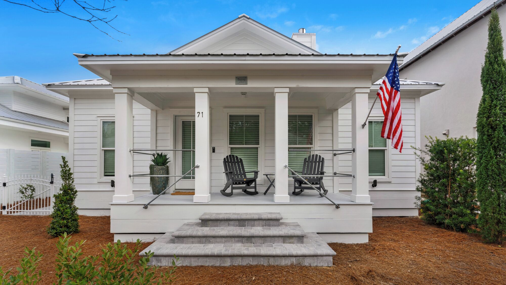 A white house with a front porch, two rocking chairs, and an American flag.