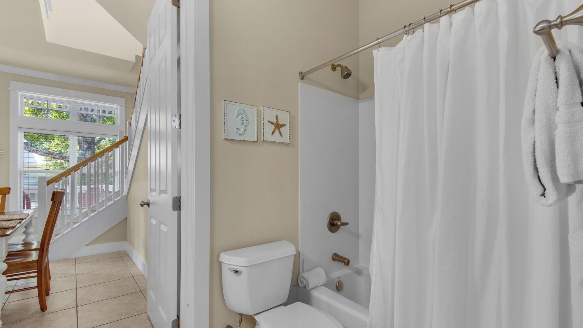A bathroom with a toilet, bathtub, and shower curtain. There is a staircase leading to another room.