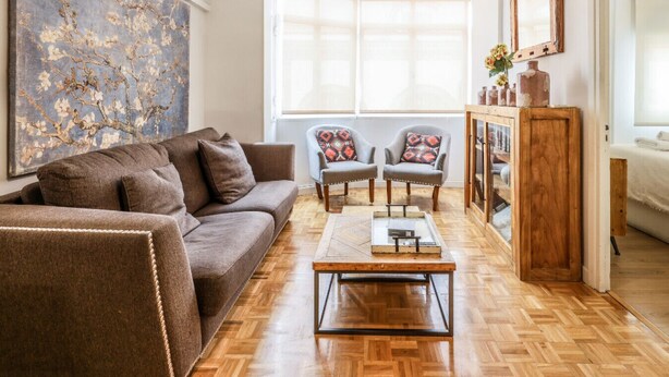 Een woonkamer met een bruine bank, twee fauteuils, een salontafel en een houten kast.