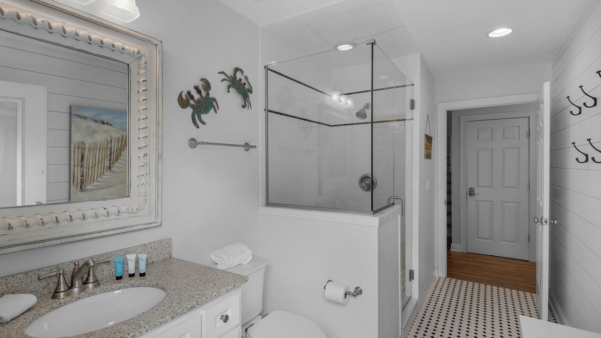 A bathroom with a large mirror, a sink with toiletries, a toilet, and a glass-enclosed shower.