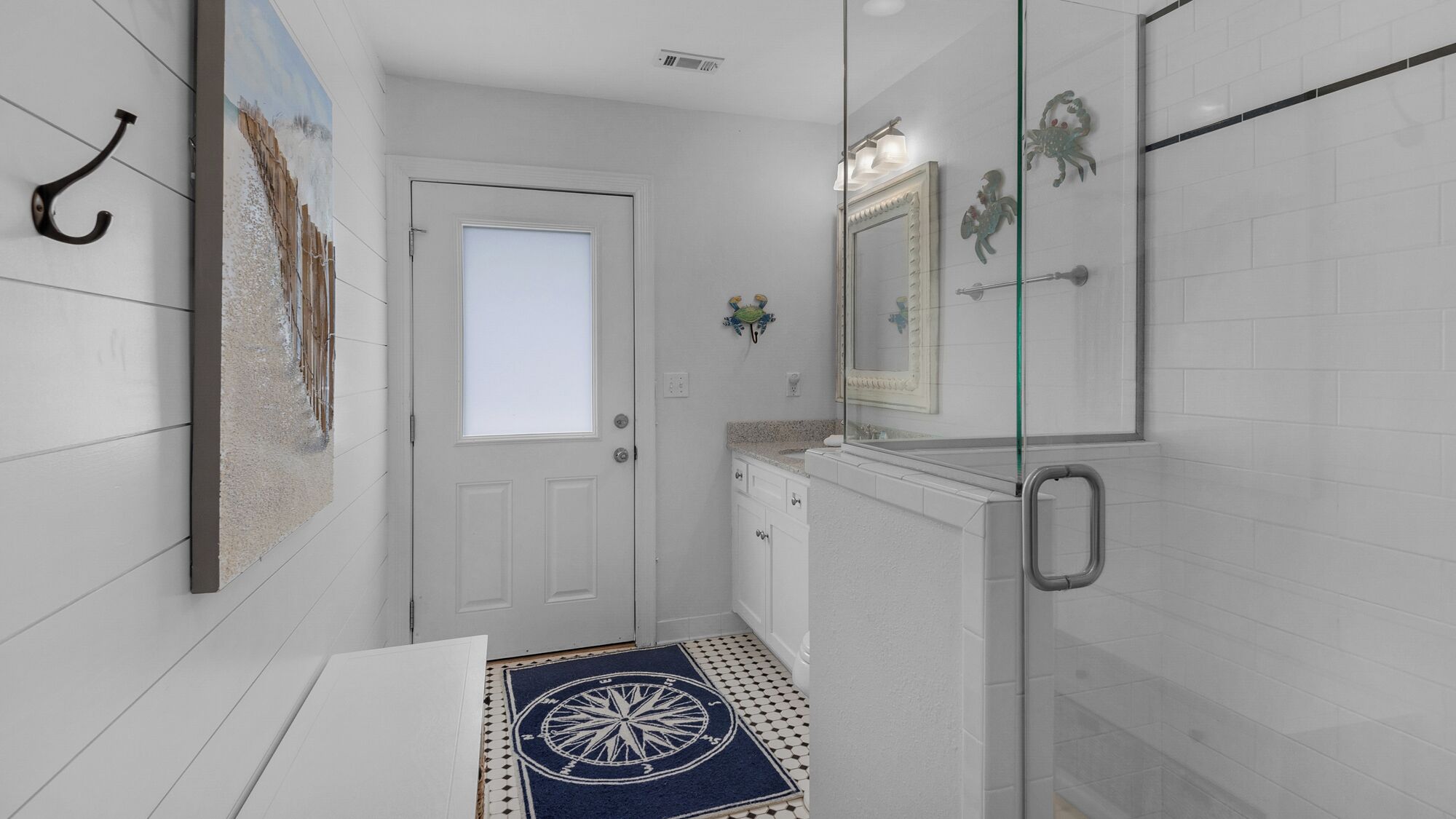 A bathroom with a white door, a glass shower enclosure, a sink with a mirror, and a decorative rug.