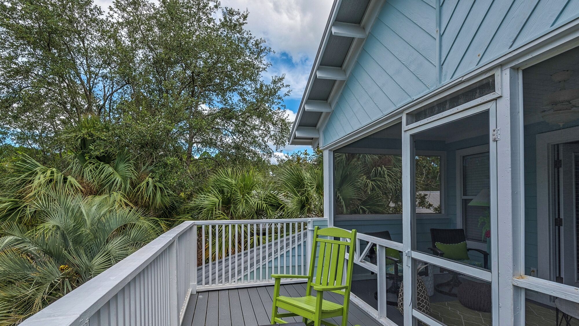 A covered outdoor area with a white railing, a green chair, and a view of a house with a blue exterior.