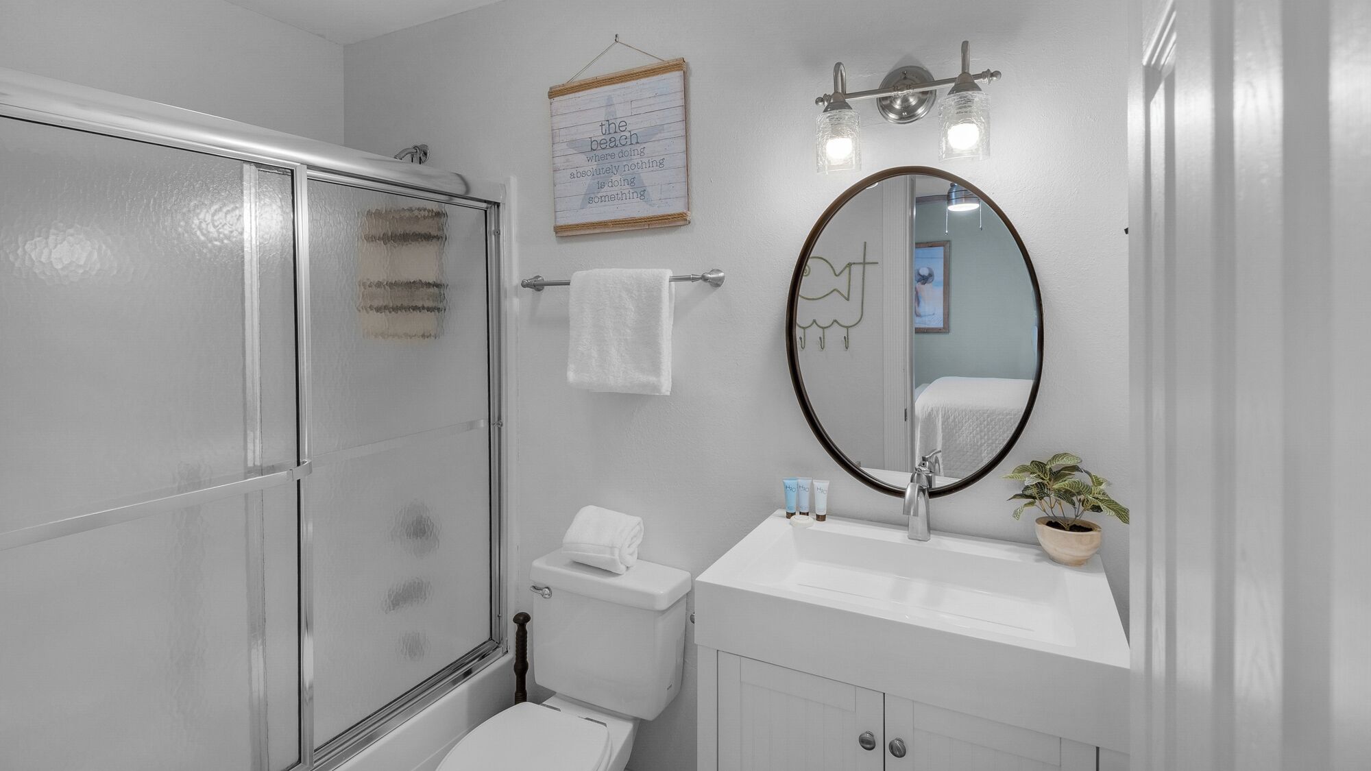 Een badkamer met een douchecabine van glas, een toilet, een wastafel met spiegel en een handdoekrek.